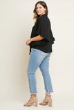 A woman modeling a black ruffled short-sleeve blouse with light-wash blue jeans and beige lace-up ankle boots, photographed against a plain light beige studio background.
