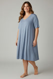 A woman modeling a light blue short-sleeve V-neck nightgown against a neutral gray studio background.