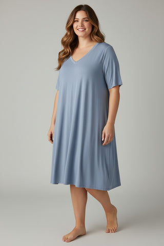 A woman modeling a light blue short-sleeve V-neck nightgown against a neutral gray studio background.