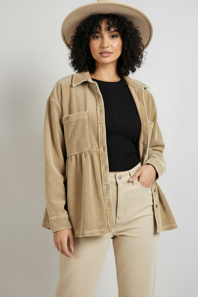 A woman modeling a beige corduroy button-up shirt jacket over a black ribbed top and beige pants, wearing a wide-brim beige hat against a light gray studio background.