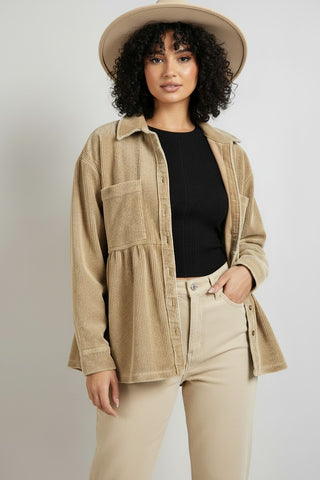 A woman modeling a beige corduroy button-up shirt jacket over a black ribbed top and beige pants, wearing a wide-brim beige hat against a light gray studio background.
