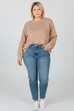 A woman modeling a beige marled knit sweater and blue jeans against a light gray studio background.