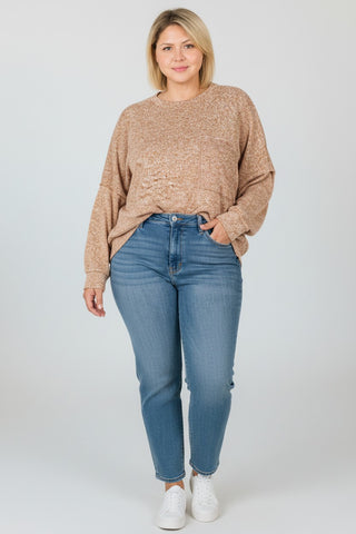 A woman modeling a beige marled knit sweater and blue jeans against a light gray studio background.