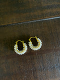 A pair of small gold hoop earrings decorated with rows of white faux pearls, resting on a dark brown wooden surface.